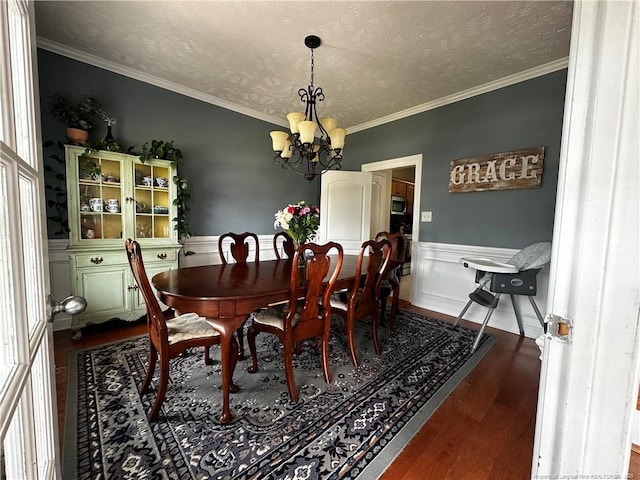 dining room with a chandelier, dark wood-type flooring, a wainscoted wall, ornamental molding, and a textured ceiling