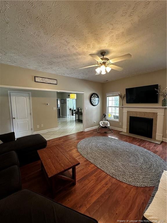 living area featuring baseboards, a textured ceiling, a fireplace with flush hearth, light wood-style flooring, and a ceiling fan