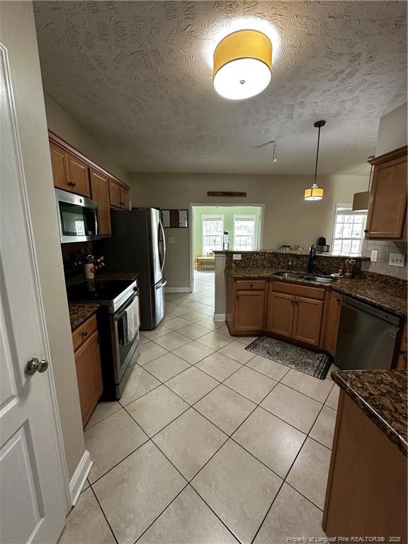 kitchen featuring stainless steel appliances, a sink, a peninsula, healthy amount of natural light, and a textured ceiling