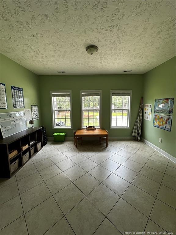 living area with a textured ceiling, tile patterned flooring, healthy amount of natural light, and baseboards