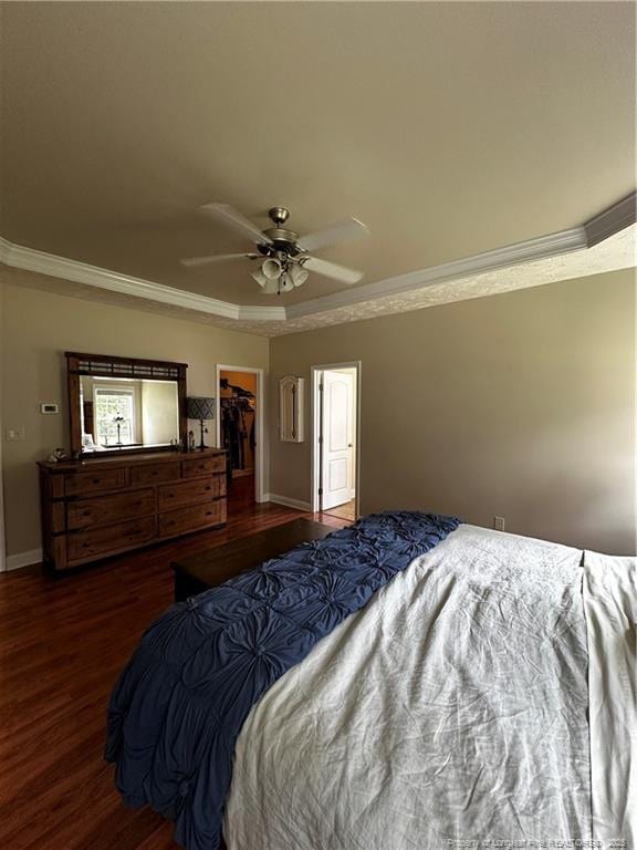 bedroom with ornamental molding, wood finished floors, a walk in closet, a ceiling fan, and baseboards