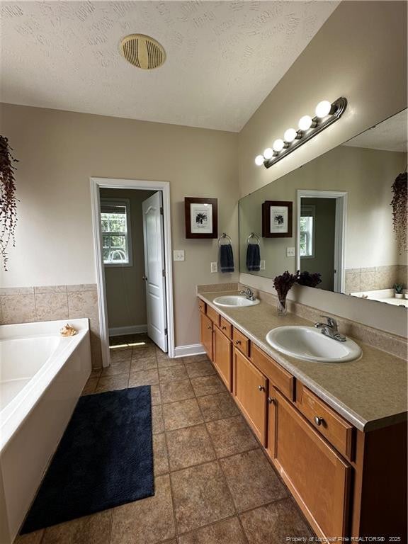 bathroom featuring a garden tub, double vanity, tile patterned flooring, and a textured ceiling