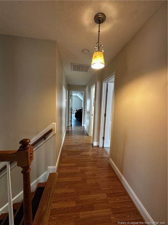 hall with wood finished floors, baseboards, and a textured ceiling