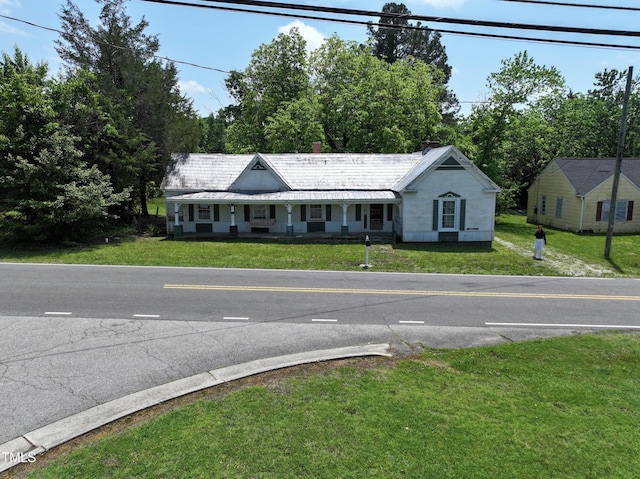 view of front facade with a front yard, covered porch, and view of scattered trees