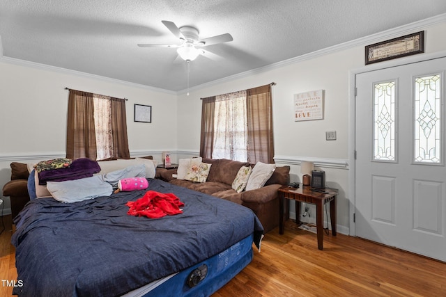 bedroom featuring crown molding, wood finished floors, wainscoting, a textured ceiling, and a ceiling fan