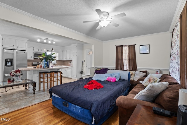 bedroom with stainless steel refrigerator with ice dispenser, ornamental molding, a wainscoted wall, a textured ceiling, and light wood-style flooring