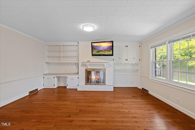 5345 Lamm Rd, Wilson, NC 27893 - unfurnished living room featuring crown molding, wood finished floors, a brick fireplace, baseboards, and built in shelves