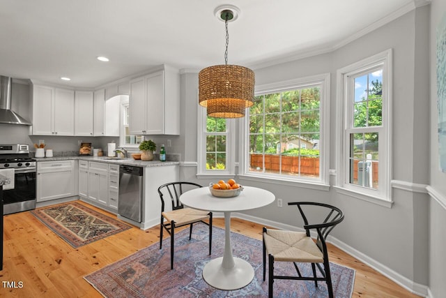 6304 Ansley Ln, Raleigh, NC 27612 - kitchen featuring appliances with stainless steel finishes, wall chimney exhaust hood, a sink, light wood-type flooring, and white cabinets