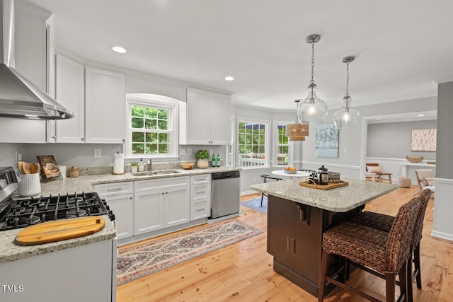 6304 Ansley Ln, Raleigh, NC 27612 - kitchen with stainless steel dishwasher, wall chimney range hood, a sink, a center island, and light wood finished floors
