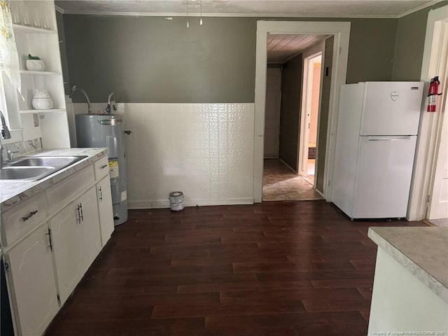 kitchen featuring water heater, freestanding refrigerator, a sink, crown molding, and dark wood-style flooring