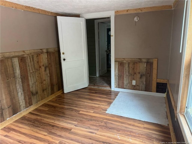 unfurnished room featuring wood finished floors, wood walls, and a textured ceiling