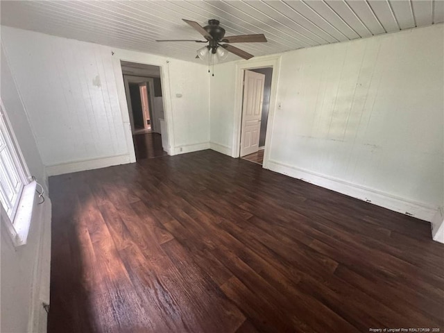 empty room featuring wood finished floors, wooden ceiling, ceiling fan, wooden walls, and baseboards