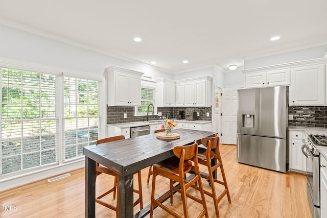 2408 Fordcrest Dr, Apex, NC 27502 - kitchen featuring stainless steel appliances, white cabinetry, decorative backsplash, light wood-style floors, and crown molding