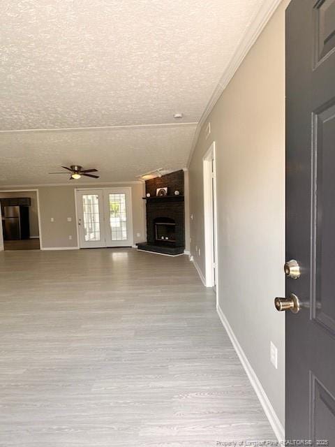 unfurnished living room with a textured ceiling, a ceiling fan, a brick fireplace, crown molding, and baseboards