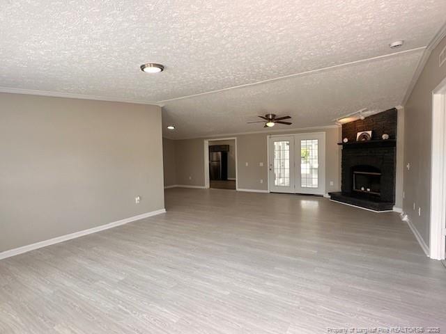 unfurnished living room featuring a textured ceiling, wood finished floors, ceiling fan, ornamental molding, and baseboards