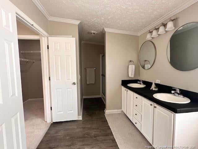 bathroom with wood finished floors, double vanity, a textured ceiling, crown molding, and a walk in closet