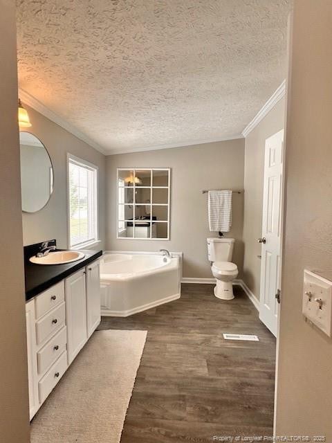 bathroom featuring ornamental molding, a textured ceiling, toilet, a bath, and wood finished floors