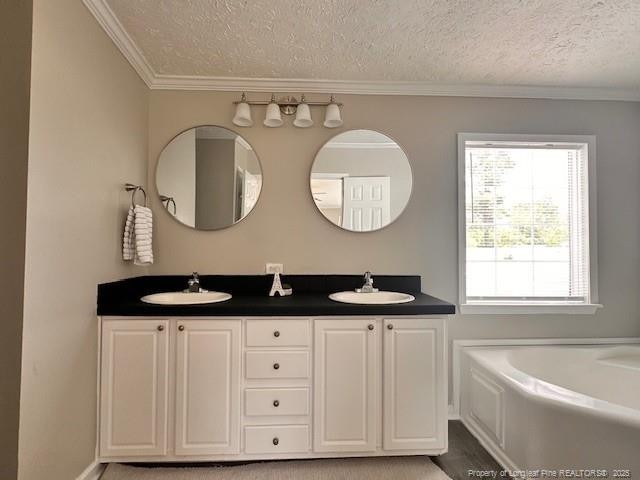 bathroom with a textured ceiling, ornamental molding, double vanity, and a tub