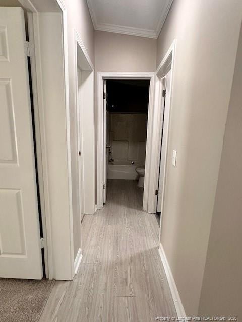 corridor featuring crown molding, light wood finished floors, and baseboards