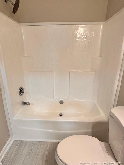 bathroom featuring toilet, wood finished floors, and  shower combination