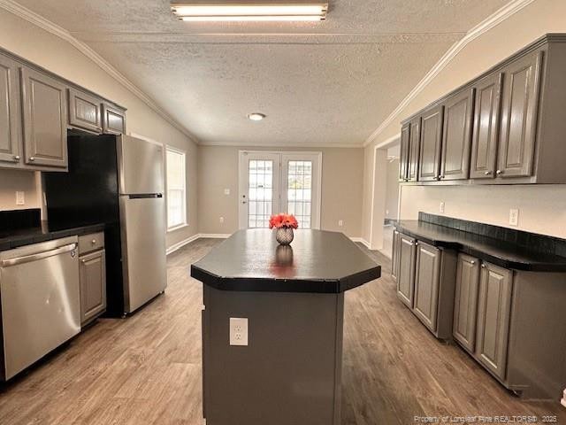 kitchen with appliances with stainless steel finishes, dark countertops, light wood finished floors, crown molding, and a center island