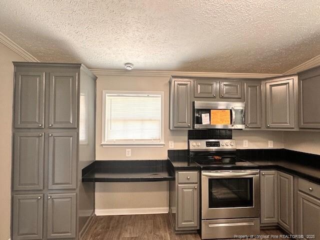 kitchen with appliances with stainless steel finishes, gray cabinetry, dark countertops, dark wood-style flooring, and ornamental molding
