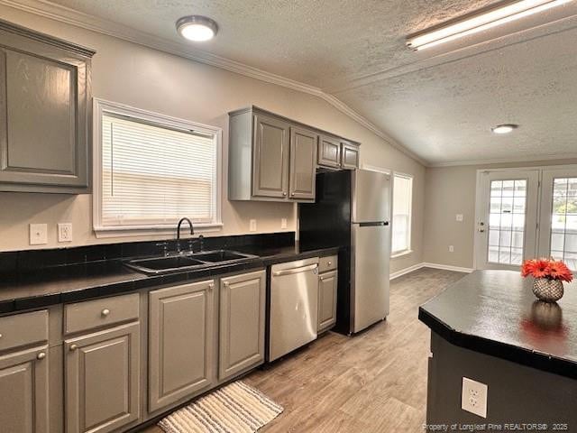 kitchen featuring stainless steel appliances, a sink, dark countertops, a textured ceiling, and lofted ceiling