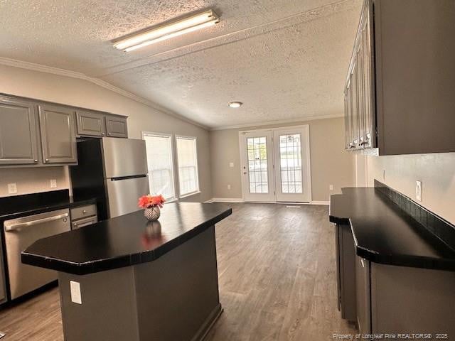 kitchen featuring stainless steel appliances, ornamental molding, dark countertops, a textured ceiling, and vaulted ceiling