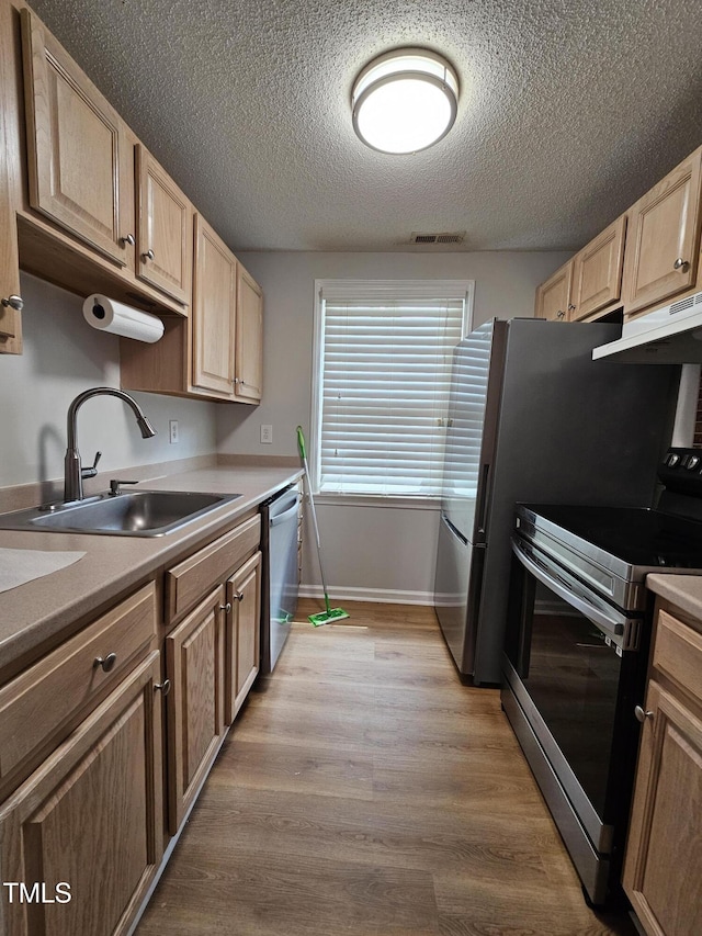 7719 Kingsberry Ct, Raleigh, NC 27615 - kitchen with stainless steel appliances, a sink, under cabinet range hood, light brown cabinetry, and a textured ceiling