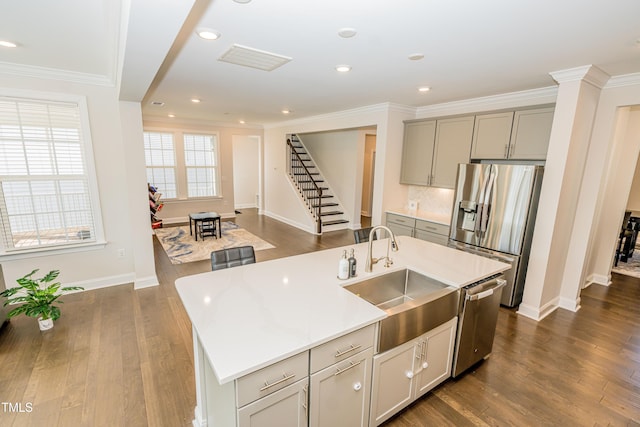 2918 Heirloom Way, Apex, NC 27502 - kitchen featuring stainless steel appliances, a sink, gray cabinetry, ornamental molding, and a center island with sink