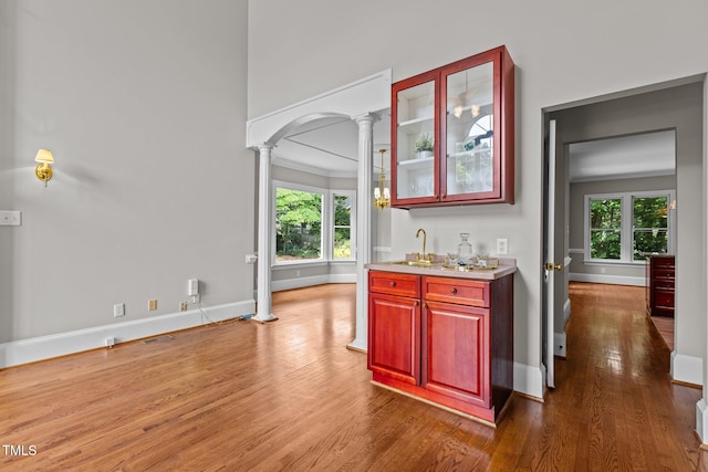 indoor wet bar featuring ornate columns, wood finished floors, healthy amount of natural light, baseboards, and ornamental molding