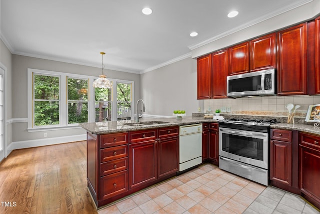 kitchen with stainless steel appliances, reddish brown cabinets, a sink, a peninsula, and backsplash