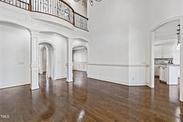 3908 Chaumont Dr, Apex, NC 27539 - unfurnished living room with arched walkways, dark wood-type flooring, a high ceiling, decorative columns, and a sink