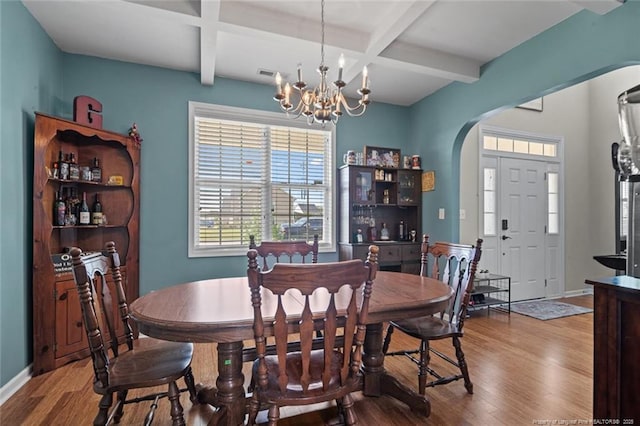 dining room with arched walkways, coffered ceiling, wood finished floors, a chandelier, and beamed ceiling