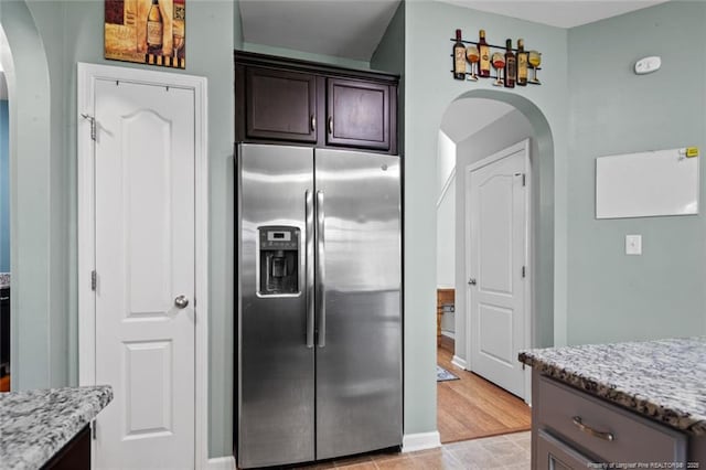 kitchen with stainless steel refrigerator with ice dispenser, arched walkways, dark brown cabinetry, and light stone counters