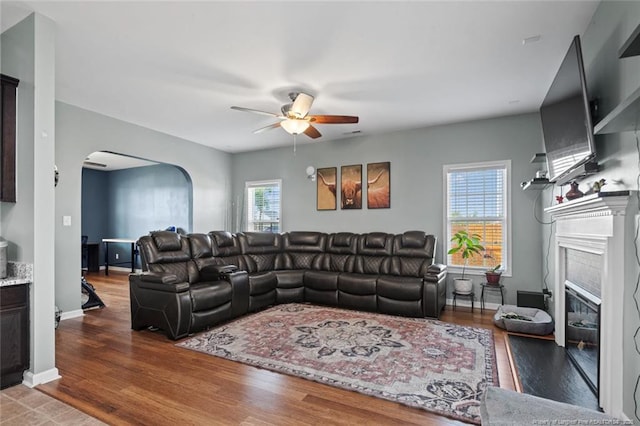 living room featuring a glass covered fireplace, arched walkways, a ceiling fan, and wood finished floors