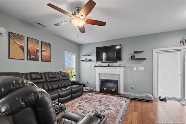 living room featuring ceiling fan, wood finished floors, and a glass covered fireplace