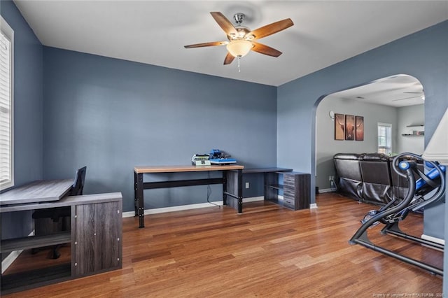 office area with ceiling fan, arched walkways, wood finished floors, and baseboards