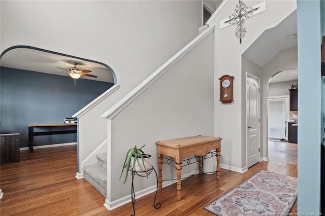 stairway featuring a ceiling fan, arched walkways, wood finished floors, and baseboards