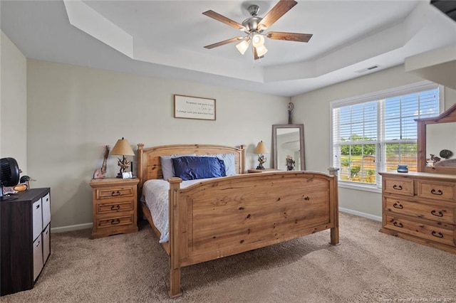 carpeted bedroom featuring a tray ceiling, baseboards, and a ceiling fan