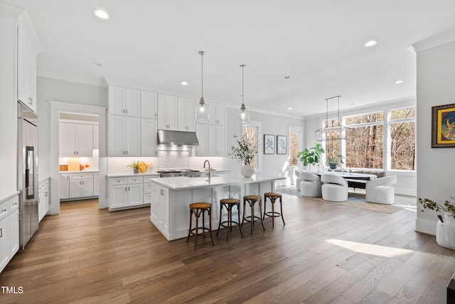 7212 Summer Tanager Trl, Raleigh, NC 27614 - kitchen with under cabinet range hood, a kitchen island with sink, light countertops, white cabinets, and recessed lighting