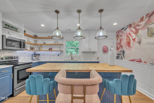 kitchen with stainless steel appliances, blue cabinets, a sink, butcher block counters, and a kitchen breakfast bar