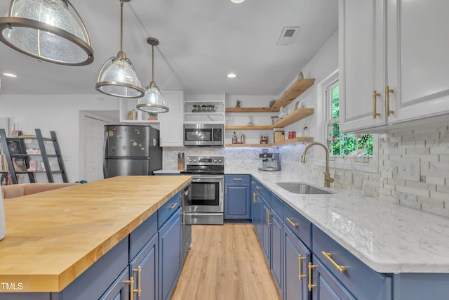 kitchen with stainless steel appliances, blue cabinets, wood counters, open shelves, and a sink