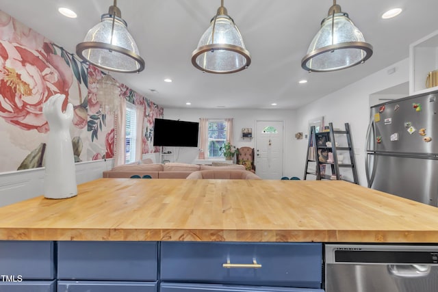 kitchen with appliances with stainless steel finishes, blue cabinetry, butcher block countertops, open floor plan, and recessed lighting