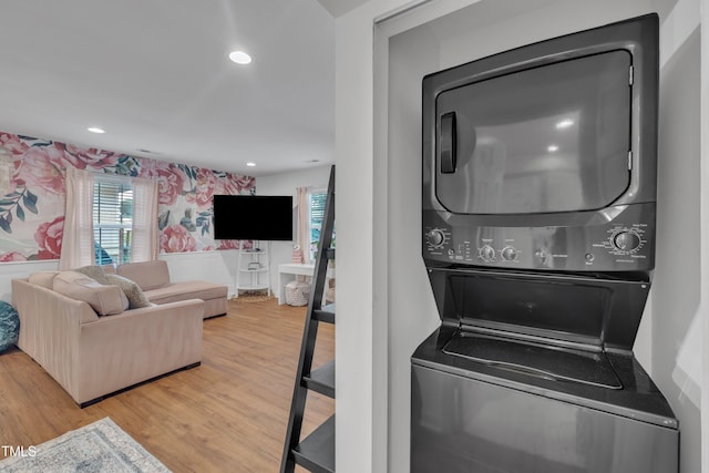 laundry room featuring stacked washer and clothes dryer, wood finished floors, wallpapered walls, and recessed lighting
