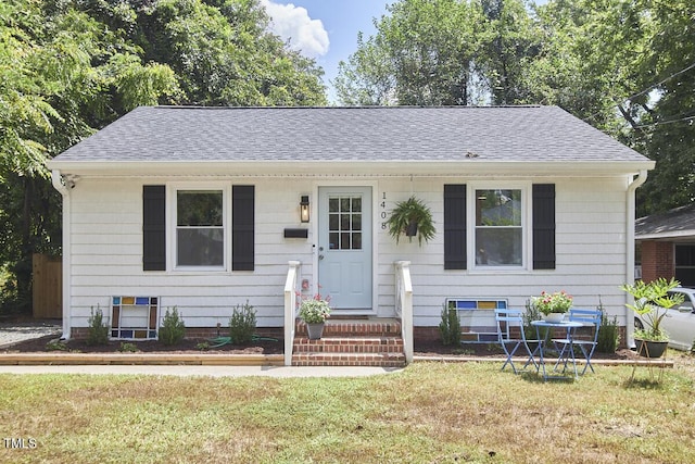 bungalow-style home featuring roof with shingles and a front lawn