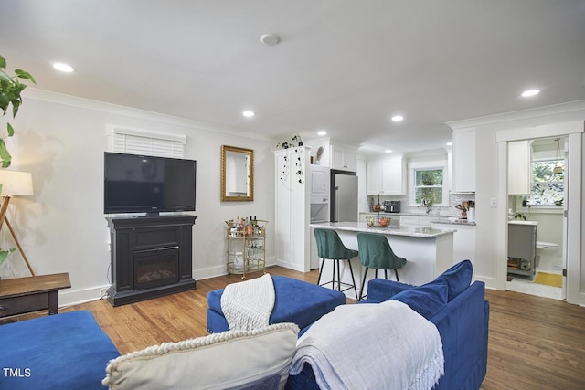 living room featuring crown molding, recessed lighting, light wood finished floors, a glass covered fireplace, and baseboards