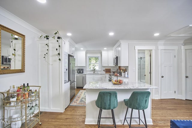 kitchen with appliances with stainless steel finishes, light wood finished floors, white cabinets, a breakfast bar area, and light stone counters