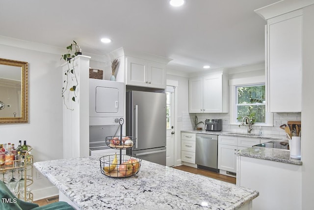 kitchen featuring stainless steel appliances, a sink, stacked washer and clothes dryer, tasteful backsplash, and light stone counters