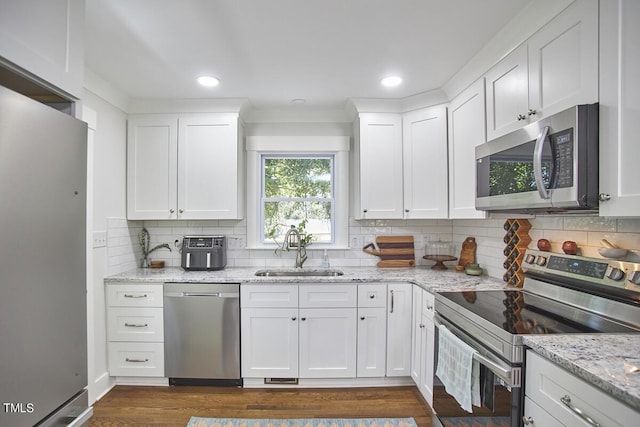 kitchen with stainless steel appliances, a sink, tasteful backsplash, white cabinetry, and dark wood finished floors